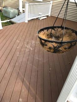 Brown deck with hanging basket, white railing, and part of a house.