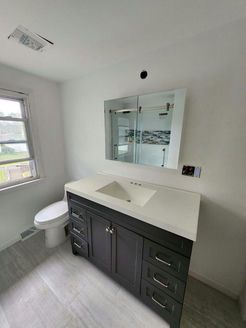 Bathroom with dark gray vanity, white countertop, and large mirror. White walls and light gray floor.