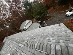 Gray shingle roof, angled view; trees, garage, driveway, and a white car in the background.