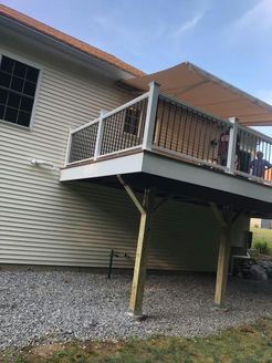 Deck with tan awning, white railing, and wooden supports, next to a beige house, gravel ground.