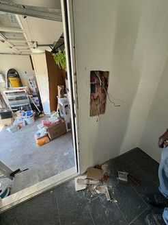 Wall with open electrical box near a doorway, debris on floor. Garage interior visible.