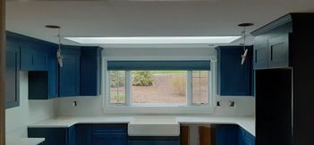 Blue kitchen with white countertops and a window with a green outdoor view.
