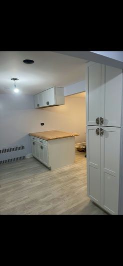 A small kitchen with white cabinets, a light-colored wood countertop, and a wooden floor.