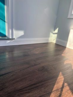 Hardwood floor in a room, with sunlight casting shadows on the wall and floor.