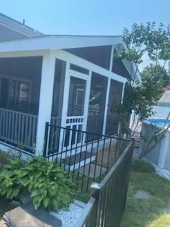 Screened porch with white trim, dark siding, black railing, and pool visible on a sunny day.