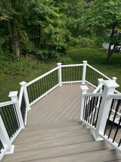 Wooden deck with white railings and black spindles, overlooking a green yard and trees.