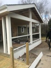 Newly constructed white porch with black railing. Man walks by with tools.
