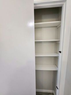 Empty white closet with built-in shelves. Door is partially open.