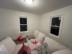 Cozy living room with beige couch, two windows, and scattered items.