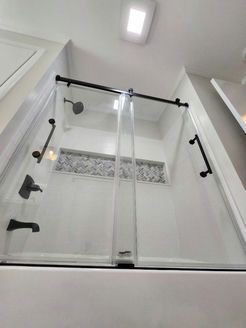 Shower with glass doors and black fixtures, featuring a built-in bench and tiled accent.