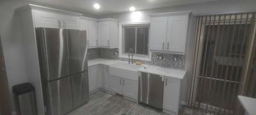 White kitchen with stainless steel appliances, cabinets, and a farmhouse sink.