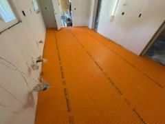 Orange, textured underlayment for flooring installed on a room's subfloor, with exposed walls and electrical outlets.