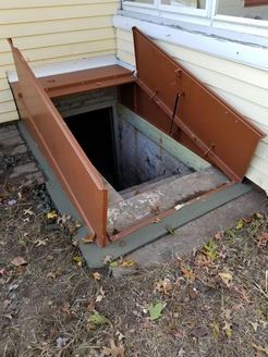 Brown metal cellar doors open to reveal steps leading into a dark basement entrance.