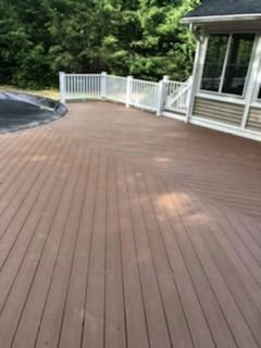 Brown wooden deck with white railing, next to a house and pool.