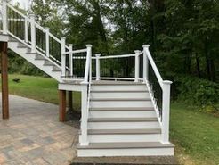 Outdoor stairway with white railings, gray steps, and black balusters, leading up to a deck.