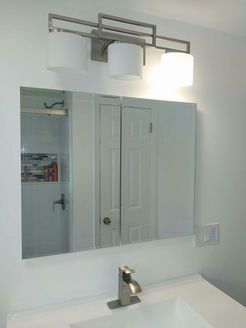 Bathroom mirror with medicine cabinet, sink, and overhead light fixture.