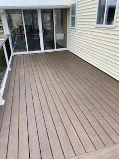 A light brown composite deck with a glass-enclosed porch and a section of a light yellow house.