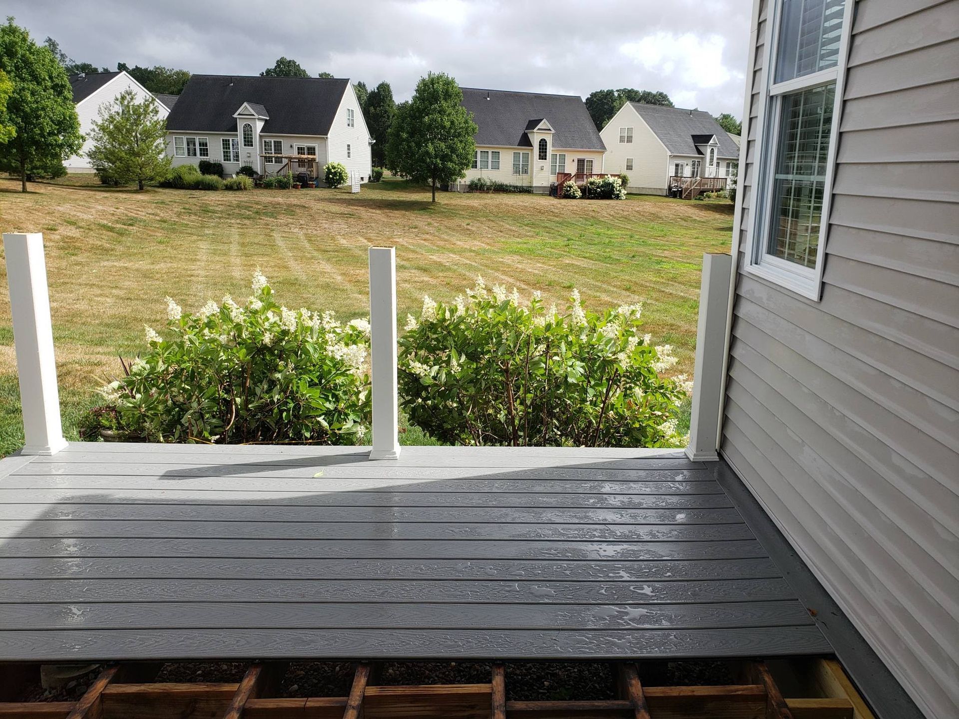Gray deck with white posts, overlooking a grassy yard and houses.