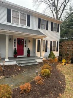 Two-story house with red front door, black shutters, and landscaping with bushes.