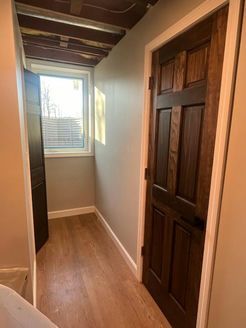 Narrow hallway with dark wooden door and window, light gray walls, and wood-look flooring.