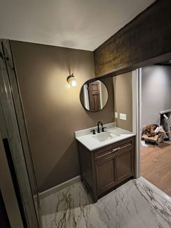 Bathroom with brown vanity, round mirror, marble floor, and sconce lighting.