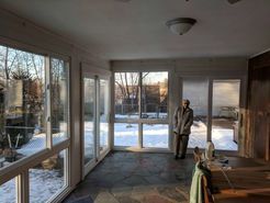 Sunroom with person standing; large windows show snowy yard, slate floor.