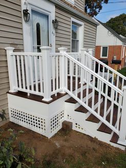 White railing and stairs leading to the front door of a house with brown siding.