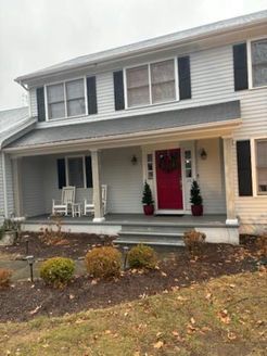 Two-story house with white siding, black shutters, red front door, and a porch with white rocking chairs.