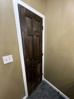 Wooden door with dark stain, white trim, and a light switch on a beige wall.