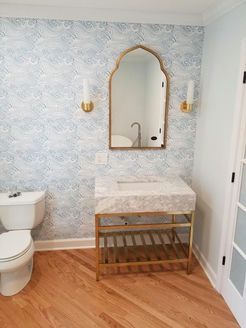 Powder room with patterned blue wallpaper, a gold-framed mirror, and a gold-legged sink.