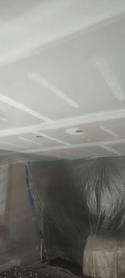 White ceiling with rectangular recesses and two recessed lights. Covered items in the lower part of the photo.