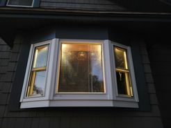Bay window of a dark house with lit-up interior visible at dusk.