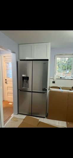 Stainless steel refrigerator with upper white cabinets. A doorway and window are visible.