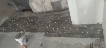 Floor tiling in progress with spacers, a bucket of materials, and protective covering.