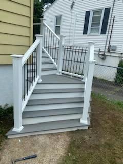 Gray and white outdoor stairs with black metal railing, leading to a house.