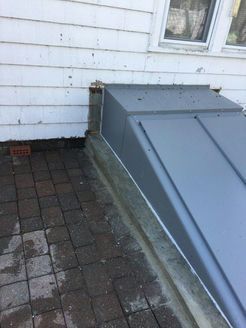 Gray cellar door next to a white house with brick pavers.