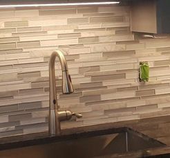 Kitchen backsplash with faucet and sink. Tile is neutral, horizontal. Faucet is silver. Green outlet cover.