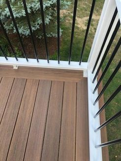 Wooden deck with brown planks and white railing with black vertical bars. Green grass in background.