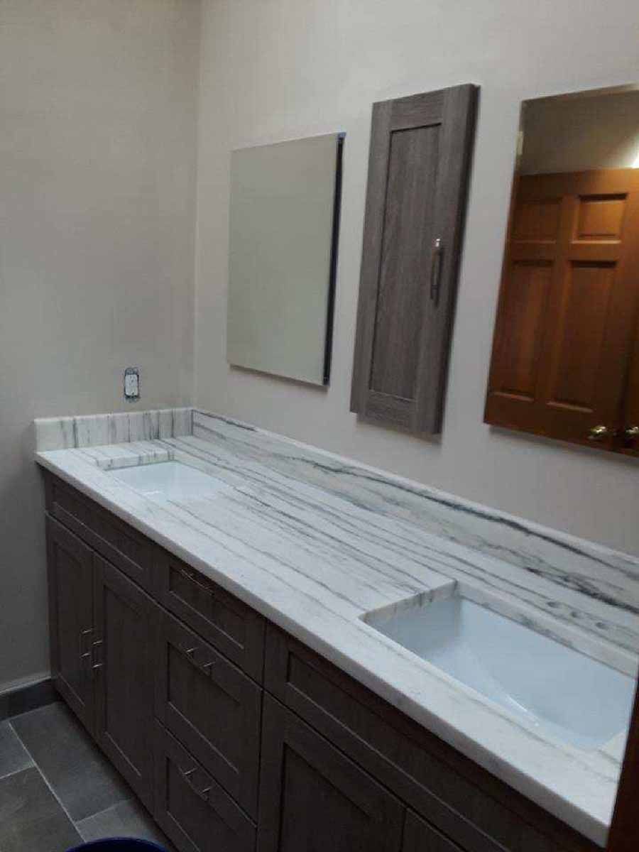 Bathroom with marble countertop, gray cabinets, two mirrors, and a cabinet.
