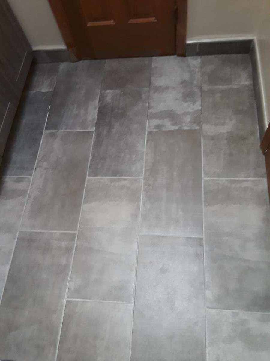Gray rectangular floor tiles in a room with a wooden door.