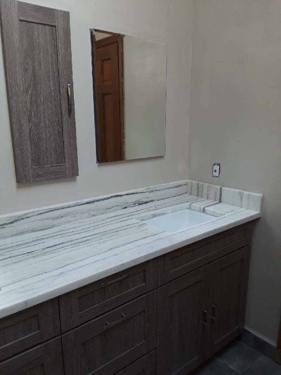 Bathroom with a marble countertop, brown cabinets, and a mirror. A wooden cabinet is on the wall.