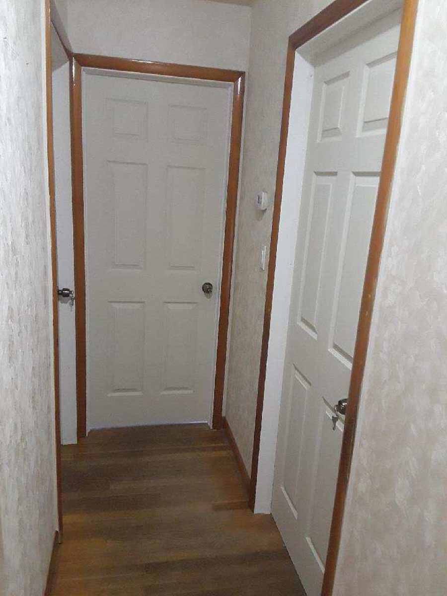 Narrow hallway with two white doors, wooden trim and floor, and patterned wallpaper.