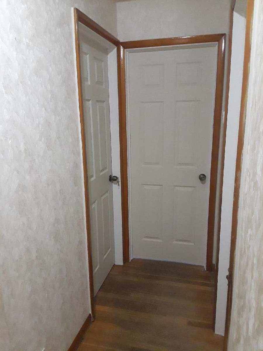 Hallway with two white doors, brown trim, wood floor, and textured wallpaper.