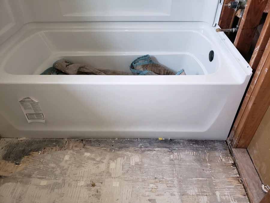 White bathtub in a room under construction, with exposed framing and damaged floor. Towels inside.