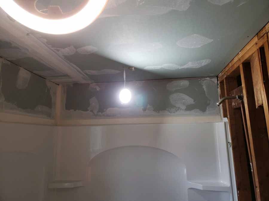 Bathroom remodel in progress with unfinished drywall and a hanging light fixture.