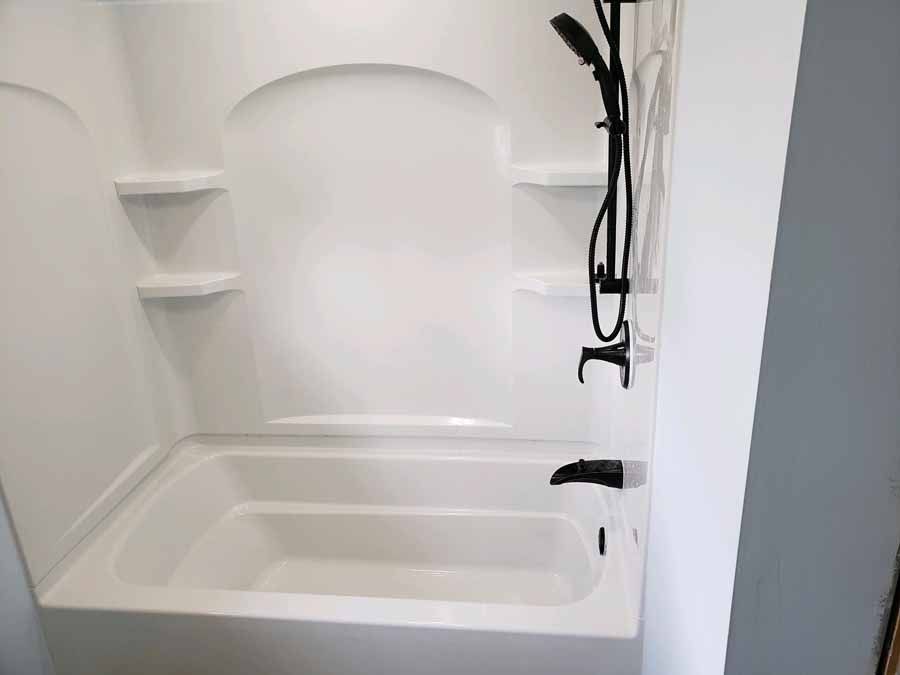 White bathtub with black shower fixture and shelving.