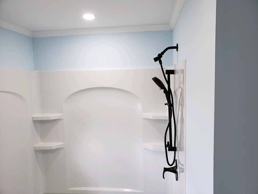White shower stall with black shower fixtures, shelves, and blue painted wall.