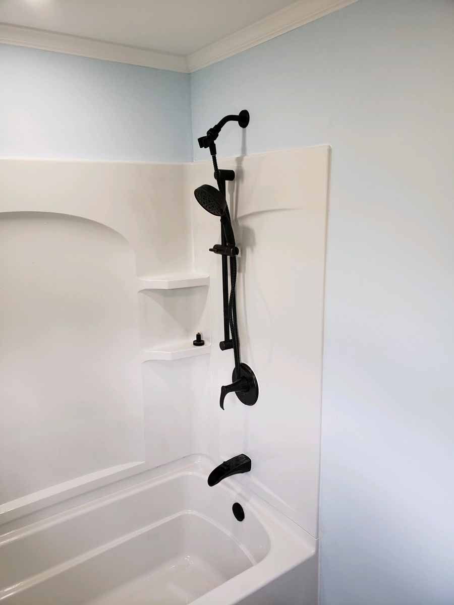 White bathtub and shower surround with black shower fixtures, set against light blue walls.