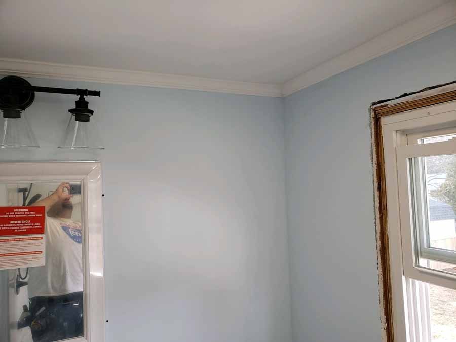 Interior of a room with blue walls, white trim, and a window; a person is reflected in the mirror.