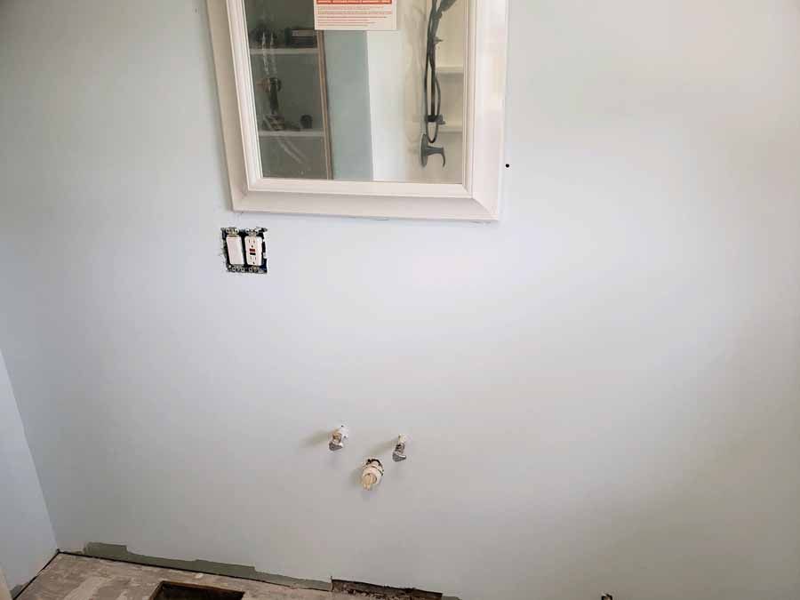 Bathroom wall with mirror, electrical outlet, and plumbing fixtures; light blue paint.
